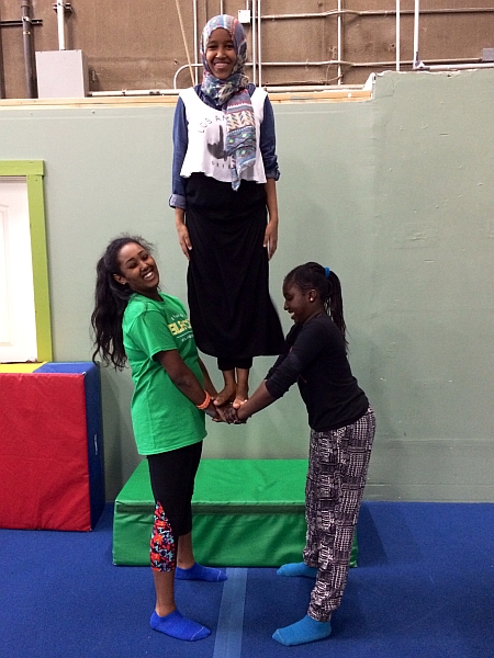 Teens from the Refugee Women's Alliance learn to work together balancing and sharing body weight in preparation for acrobatics.